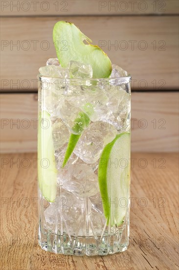 Glass of cold apple lemonade with ice on wooden table