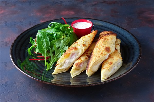 Thin pancakes stuffed with ham and melted cheese served with spinach