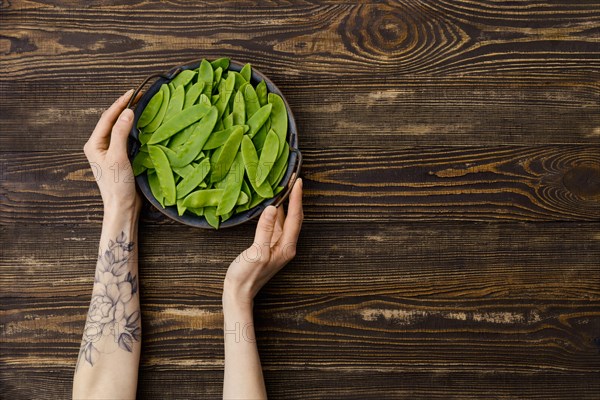 Overhead view of fresh green peas in a pods in hand over wooden background