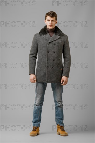 Full length portrait of handsome man in warm winter coat posing in studio