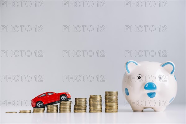 Red car driving increasing stacked coins near piggybank