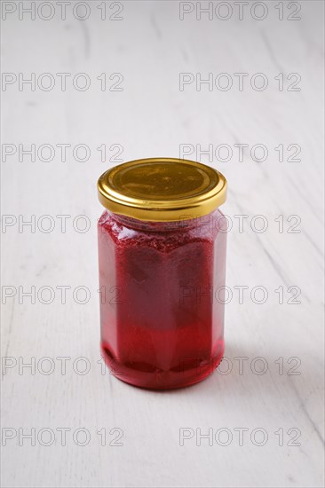 Whole closed jar of cherry jam on white wooden background