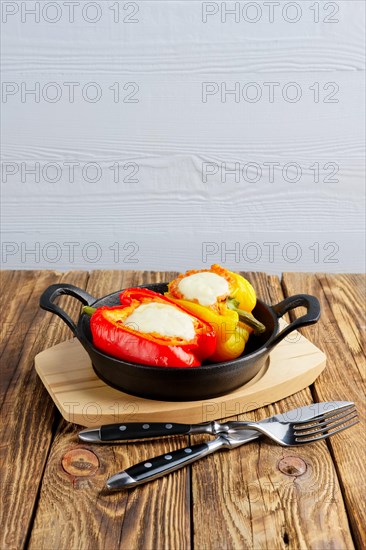 Bell pepper stuffed with meat with melted cheese mozzarella on top baked in oven in cast iron skillet. Top view. Natural wooden background