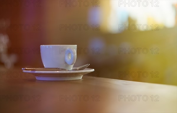 White cup of coffee with steam on wooden table near window
