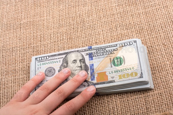 Hand holding banknote bundle of US dollar on a linen canvas background