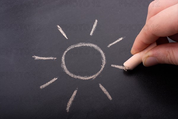 Hand drawing sun by chalk with light ray shape on blackboard background