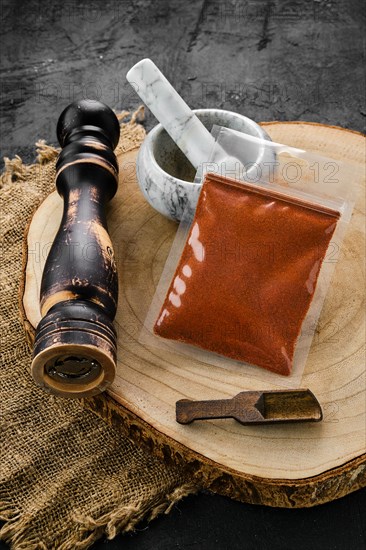 Wooden cross section with chilli pepper in plastic package and stone mortar and mill