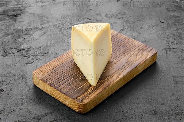 Triangular piece of goat cheese on wooden cutting board on black background