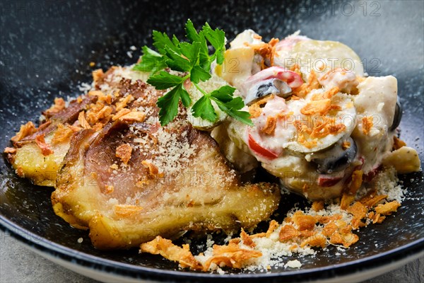 Closeup view of pickled cucumber with boiled potato and olives served with fried pork belly slices on a plate