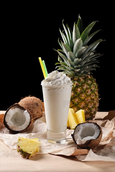 Selective focus composition with coconut cocktail served with pineapple and coconuts on rough paper over the wooden table