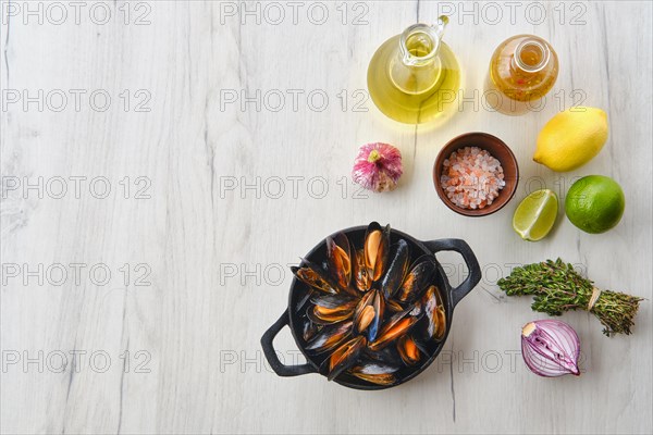 Top view of unpeeled mussels in cast iron skillet with spice and herbs