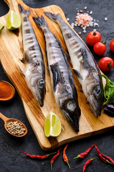 Raw fresh icefish on wooden cutting board with spice and herbs