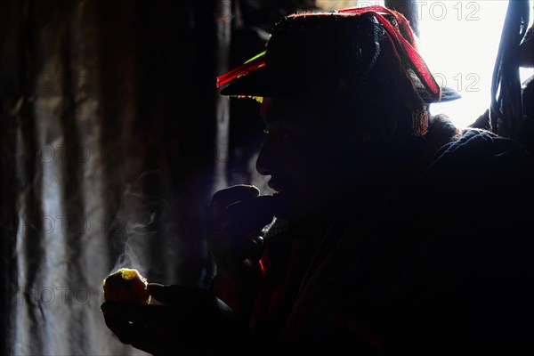 Silhouette of a Quechua Indian in traditional dress eating a hot potato