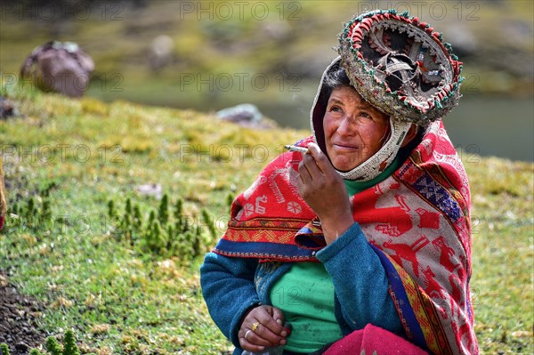 Quechua Indian woman in traditional dress sitting in a meadow smoking at Pacha Mama ceremony