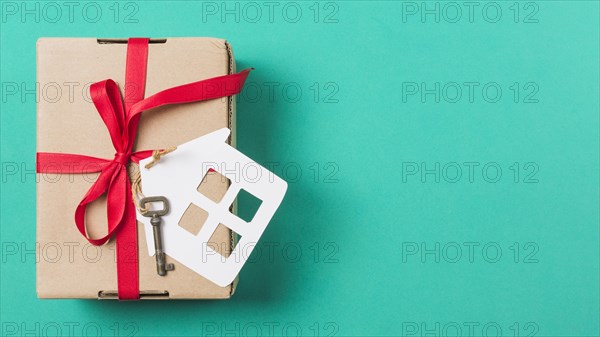 Brown gift box tied with red ribbon house key turquoise surface