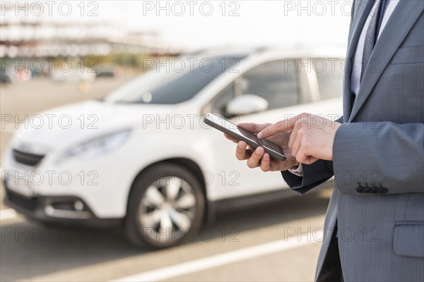 Businessman with smartphone in front of car