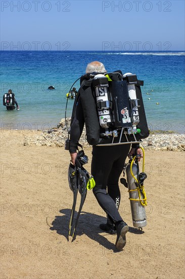 Diver with scuba equipment for technical diving tech diving rebreather goes over beach to sea
