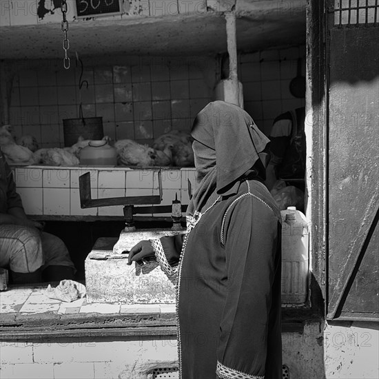 Traditionally dressed Muslim woman with niqab stands at poultry stall