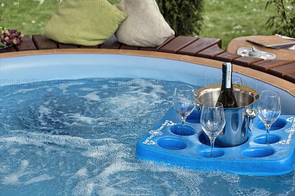 Tray with champagne bucket and three glasses floating in a pool in the garden