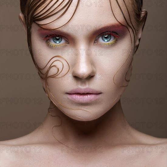 Beautiful girl with bright colored makeup and wet strands of hair on the face. Creative image. Picture taken in the studio