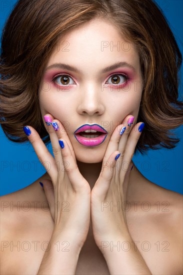 Beautiful model girl with bright makeup and colored nail polish. Beauty face. Short colorful nails. Picture taken in the studio on a blue background