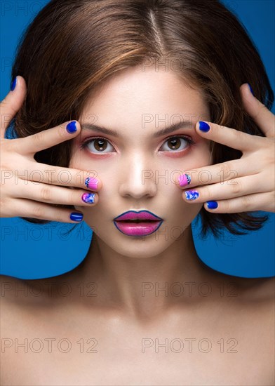 Beautiful model girl with bright makeup and colored nail polish. Beauty face. Short colorful nails. Picture taken in the studio on a blue background