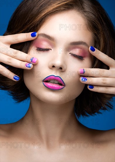 Beautiful model girl with bright makeup and colored nail polish. Beauty face. Short colorful nails. Picture taken in the studio on a blue background