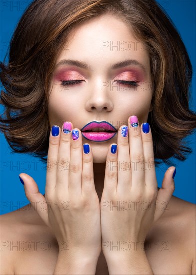 Beautiful model girl with bright makeup and colored nail polish. Beauty face. Short colorful nails. Picture taken in the studio on a blue background