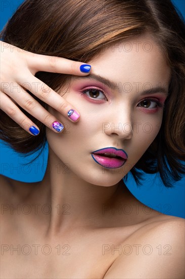 Beautiful model girl with bright makeup and colored nail polish. Beauty face. Short colorful nails. Picture taken in the studio on a blue background