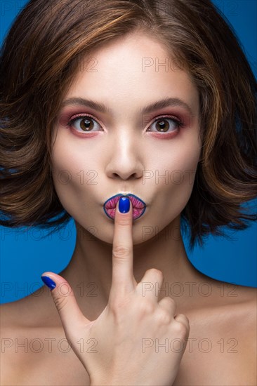 Beautiful model girl with bright makeup and colored nail polish. Beauty face. Short colorful nails. Picture taken in the studio on a blue background