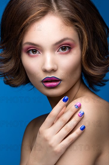 Beautiful model girl with bright makeup and colored nail polish. Beauty face. Short colorful nails. Picture taken in the studio on a blue background