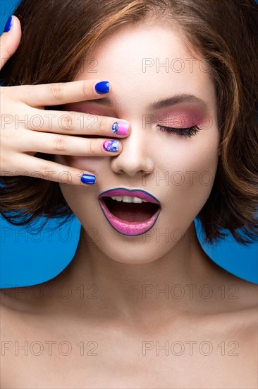 Beautiful model girl with bright makeup and colored nail polish. Beauty face. Short colorful nails. Picture taken in the studio on a blue background