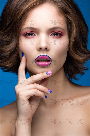 Beautiful model girl with bright makeup and colored nail polish. Beauty face. Short colorful nails. Picture taken in the studio on a blue background