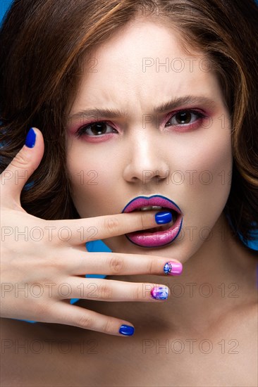 Beautiful model girl with bright makeup and colored nail polish. Beauty face. Short colorful nails. Picture taken in the studio on a blue background