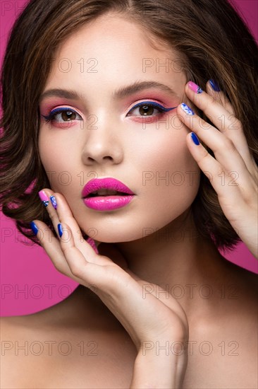 Beautiful model girl with bright makeup and colored nail polish. Beauty face. Short colorful nails. Picture taken in the studio on a pink background