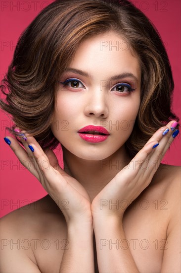 Beautiful model girl with bright makeup and red heart in the hands. Beauty face. Short colorful nails. Picture taken in the studio on a red background