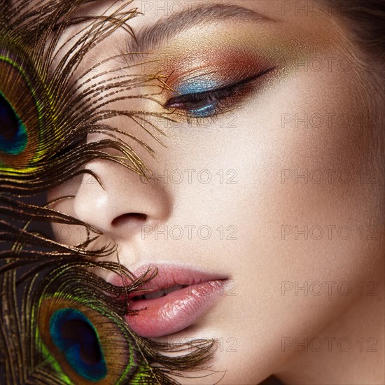 Beautiful girl with bright colored makeup and peacock feather on her face. Beauty face. Close-up. Photos shot in the studio