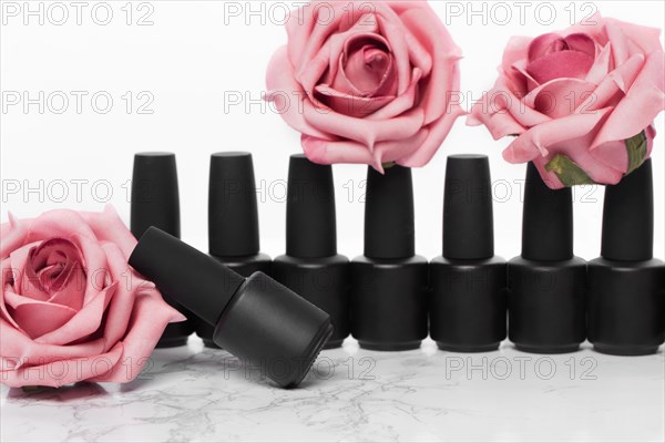 Black bottles of nail polish on a background of flowers. Manicure design