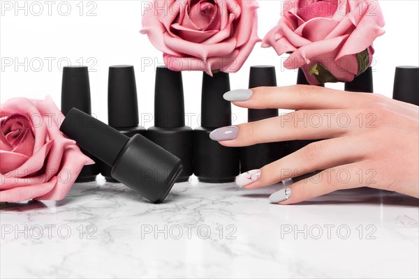 Black bottles of nail polish on a background of flowers. Manicure design