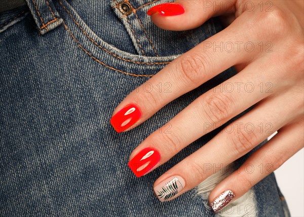 Bright neon red manicure on female hands on the background of jeans. Nail design. Beauty hands