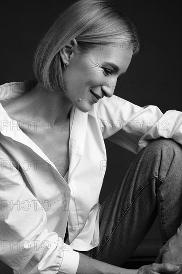 Beautiful blonde woman in a white shirt posing in the studio on a black background. Black and white photo. Model Tests
