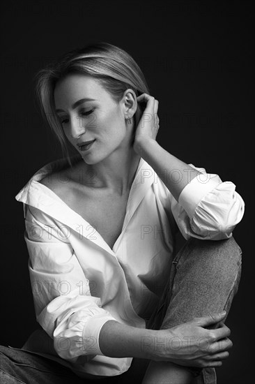 Beautiful blonde woman in a white shirt posing in the studio on a black background. Black and white photo. Model Tests