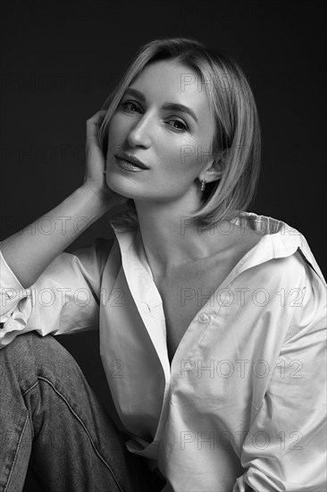 Beautiful blonde woman in a white shirt posing in the studio on a black background. Black and white photo. Model Tests