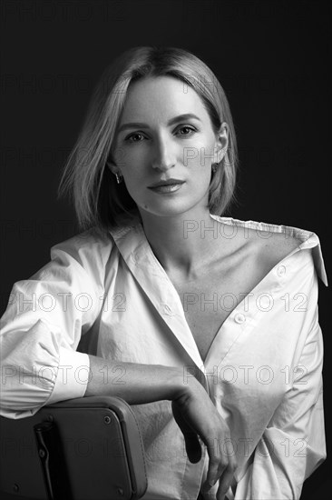 Beautiful blonde woman in a white shirt posing in the studio on a black background. Black and white photo. Model Tests