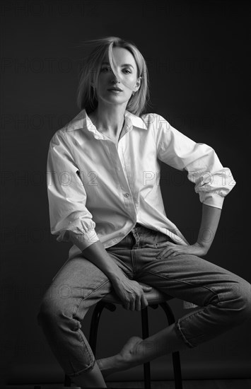 Beautiful blonde woman in a white shirt posing in the studio on a black background. Black and white photo. Model Tests