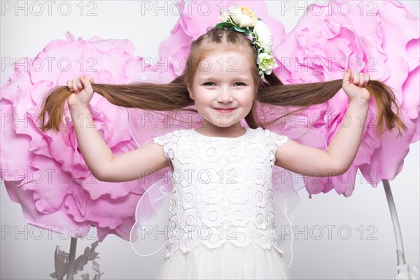 Little fairy girl in white dress on a background of flowers. Photo taken in studio