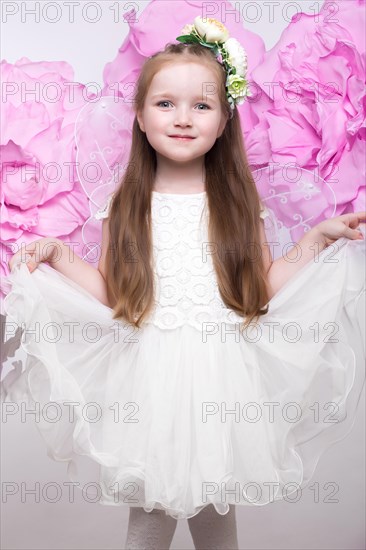 Little fairy girl in white dress on a background of flowers. Photo taken in studio