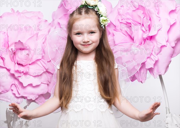 Little fairy girl in white dress on a background of flowers. Photo taken in studio