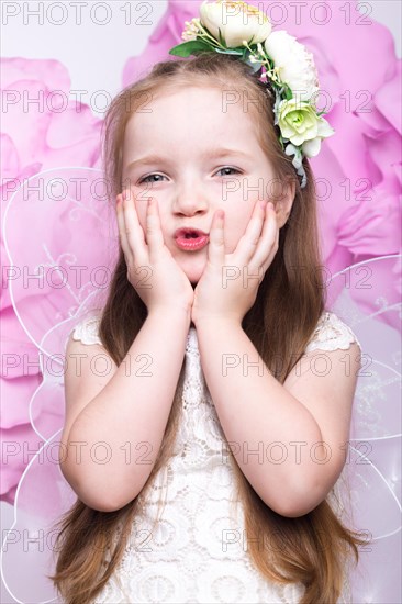 Little fairy girl in white dress on a background of flowers. Photo taken in studio