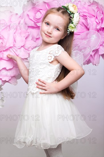 Little fairy girl in white dress on a background of flowers. Photo taken in studio